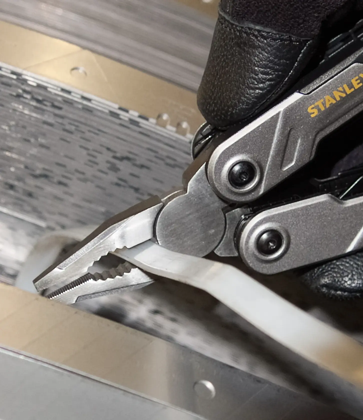 Foto von STANLEY FMHT0-72414 Multitool-Zange, die ein Kabelband in industrieller Umgebung hält.