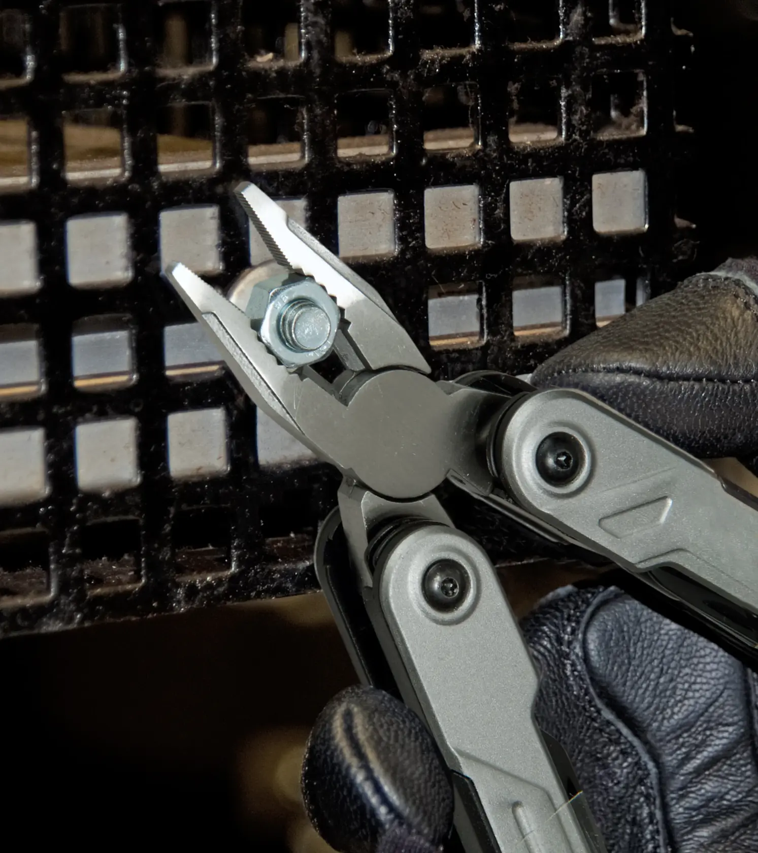 STANLEY FMHT0-72414 Multitool-Zange mit Schraube, Nahaufnahme, Handschuh, schwarzer Gitterhintergrund.