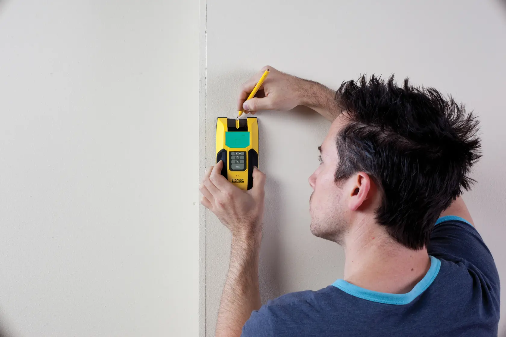 STANLEY FMHT0-77407 Ortungsgerät an Wand, Nutzer markiert Punkt mit Bleistift, Produktfoto.
