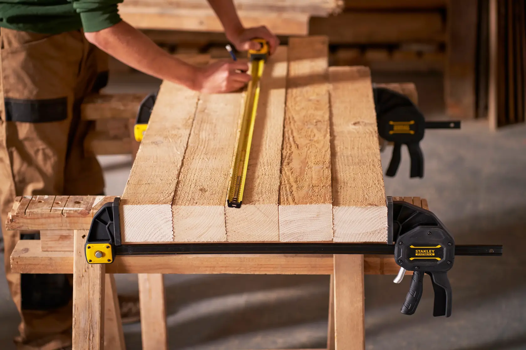 STANLEY FMHT0-83240 Stangenzwingen fixieren Holzplanken auf Werkbank, Person misst mit Maßband.