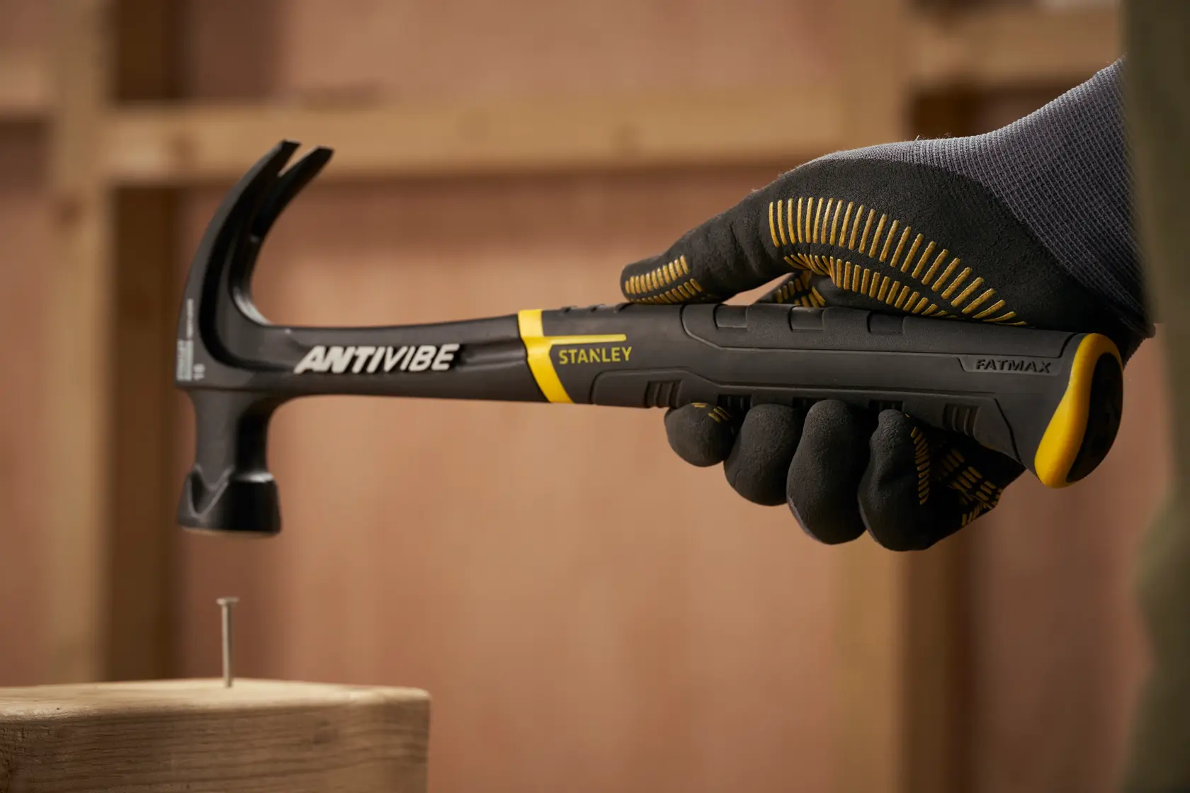STANLEY FMHT1-51275 Klauenhammer mit schwarz-gelbem Griff, gehalten von einer behandschuhter Hand, FATMAX ANTIVIBE-Serie.