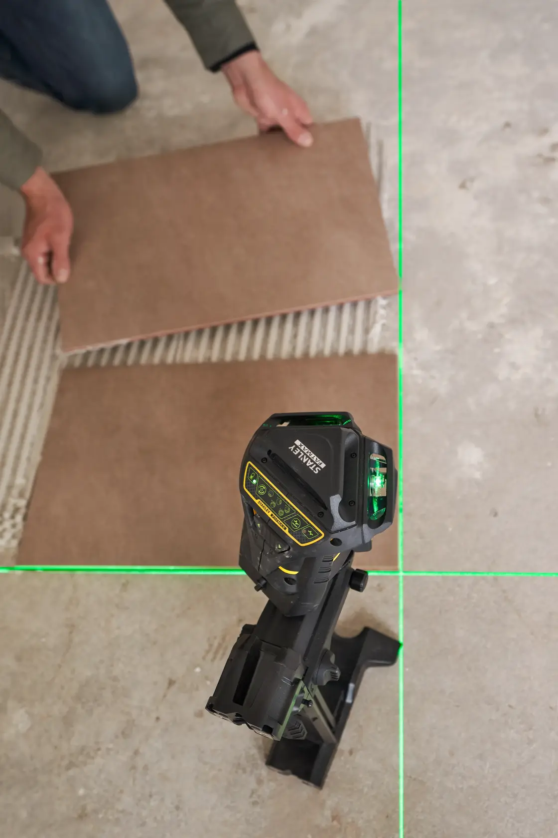 Foto des STANLEY FMHT1-77356 Laser-Levels, das grüne Linien beim Verlegen von Fliesen auf den Boden projiziert.