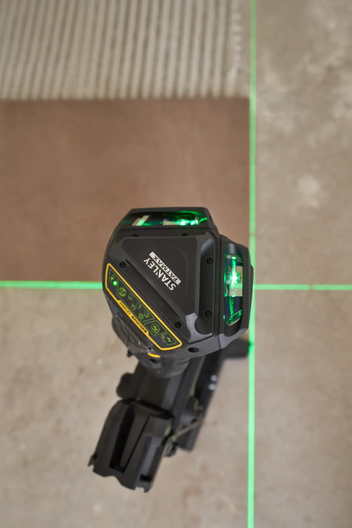 STANLEY FMHT1-77356 grüne Laser-Wasserwaage projiziert Linien auf Fliesenboden, Draufsicht.