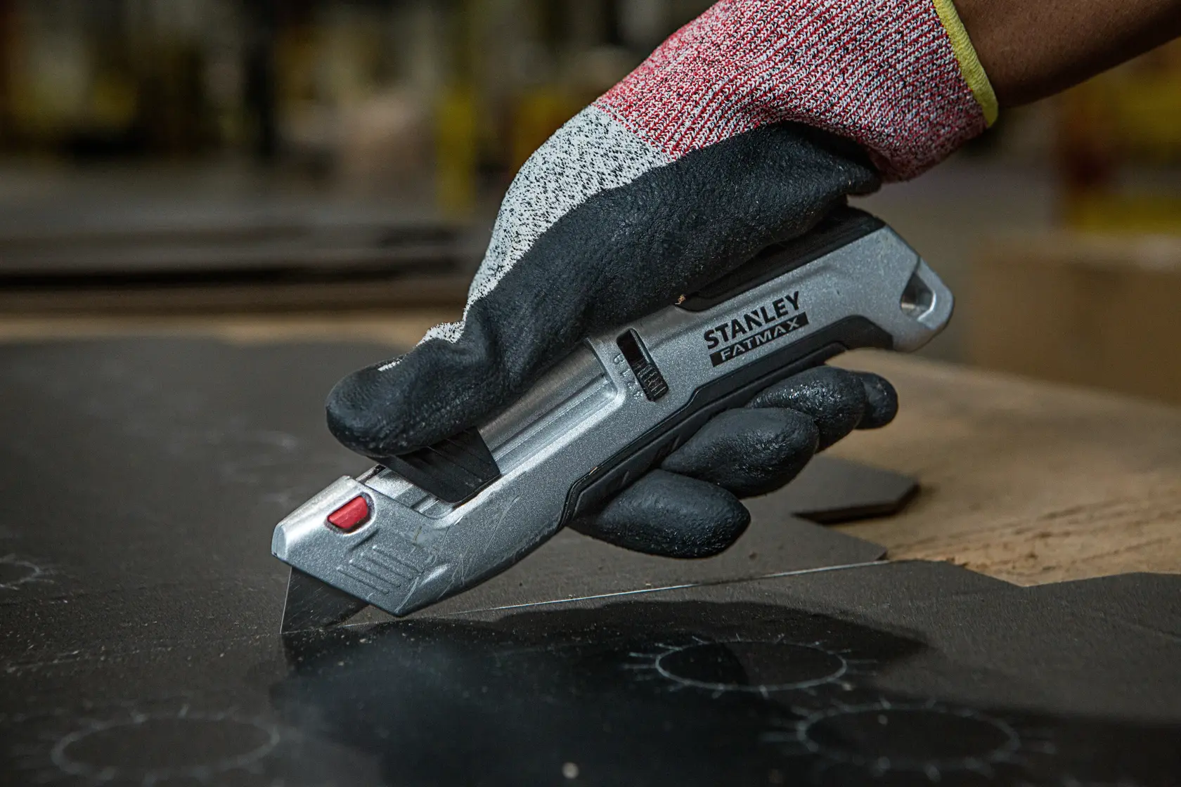 Foto des STANLEY FMHT10367-0 Universalmessers in behandschuhter Hand beim Schneiden von schwarzem Material.