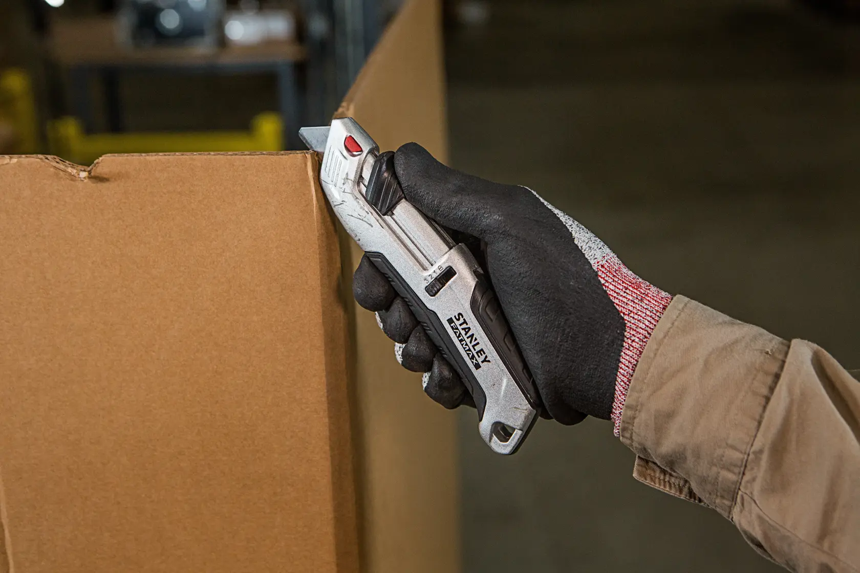 Stanley FMHT10367-0 Messer schneidet Karton, gehalten in behandschuhter Hand, Produkt in Anwendung.