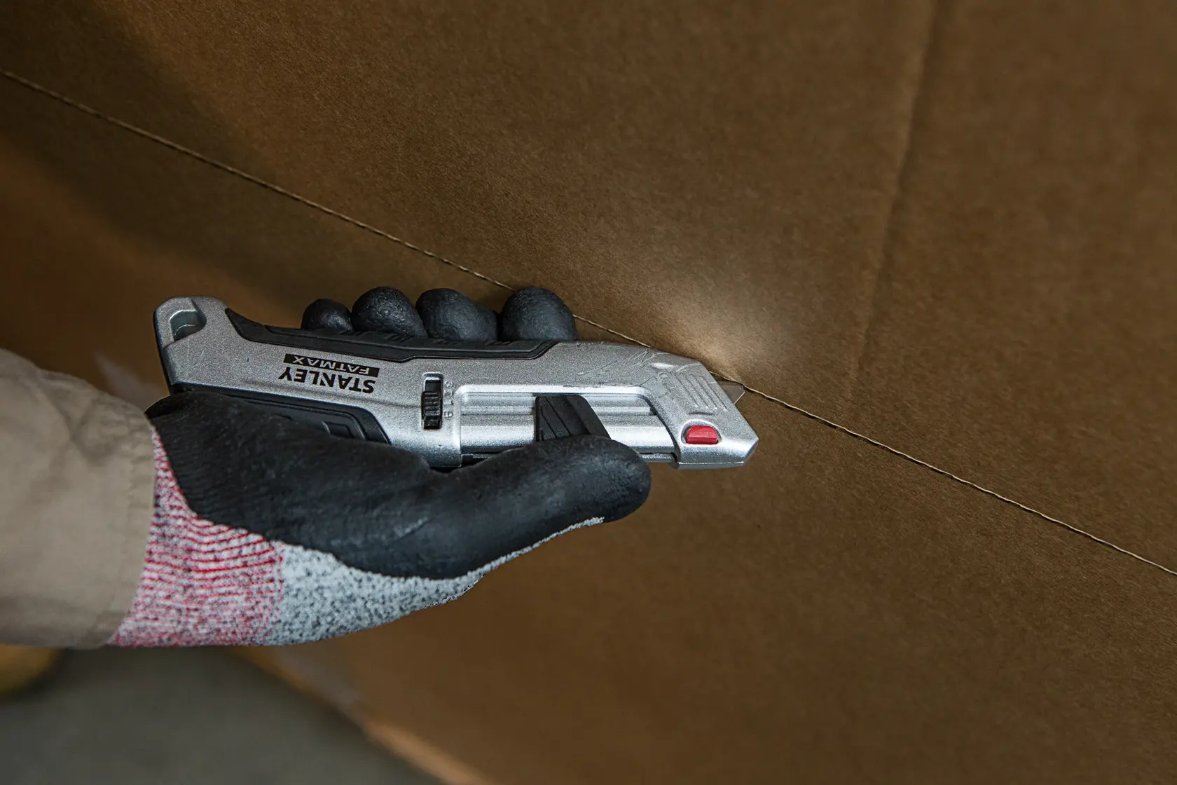 STANLEY FMHT10367-0 Universalmesser schneidet Karton, Nahaufnahme einer Hand mit dem Werkzeug.