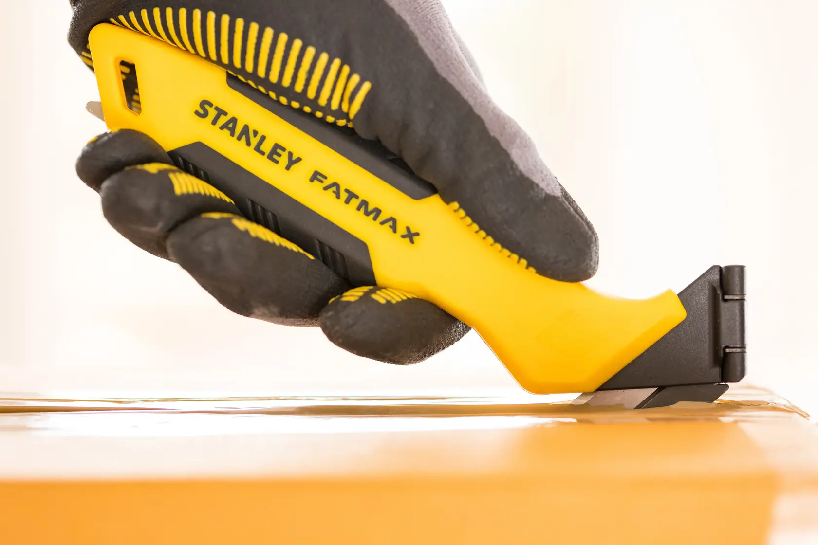 STANLEY FMHT10373-0 Cuttermesser in behandschuhtem Hand schneidet Klebeband, gelb-schwarz, Seitenansicht.