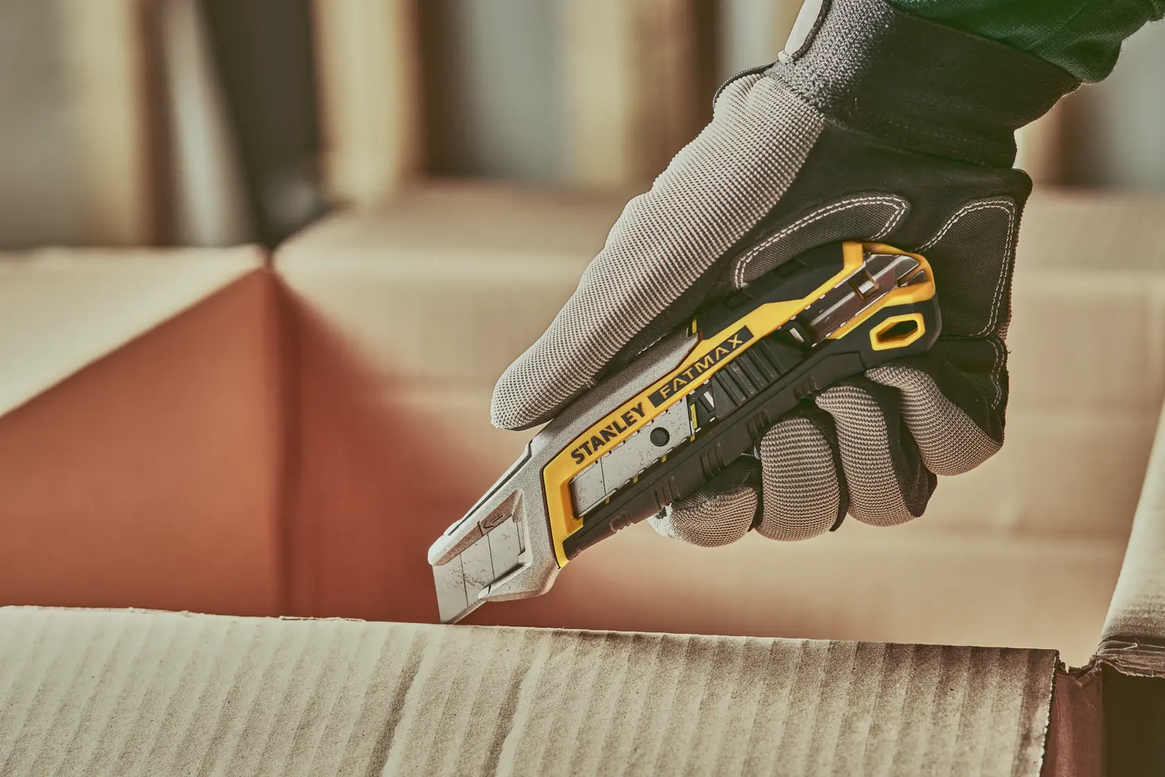 Foto des STANLEY FMHT10594-0 Universalmessers schneidet Karton, Arbeiter trägt grauen Schutzhandschuh.