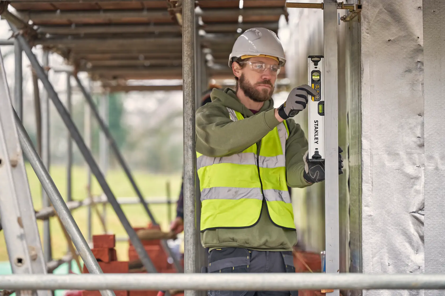 Arbeiter verwendet STANLEY FMHT43670-1 Wasserwaage auf Baustelle, trägt Warnweste und Helm.