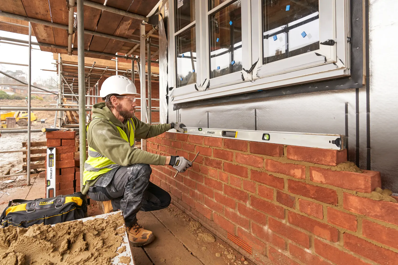 STANLEY FMHT43679-1 Wasserwaage von einem Bauarbeiter an einer Ziegelwand auf einer Baustelle, Seitenansicht.