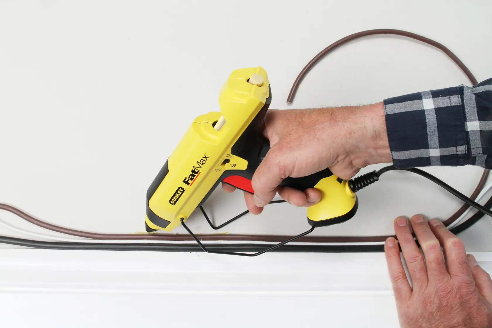 STANLEY FMHT6-70418 gelbe FastMax Heißklebepistole beim Verlegen von Kabeln an einer Wand.
