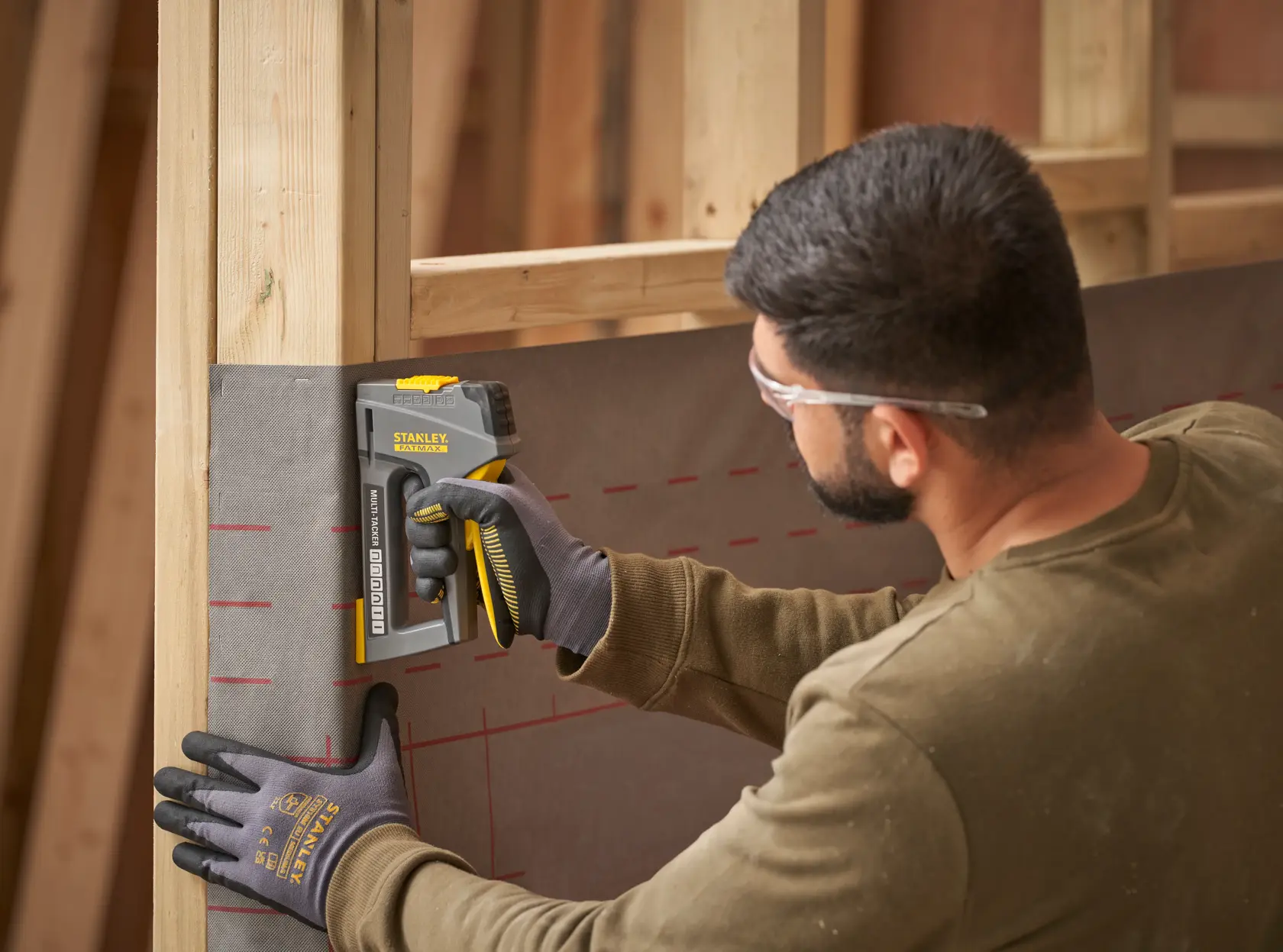 STANLEY FMHT6-70868 Hochleistungs-Tacker befestigt Material an Holzrahmen, Seitenansicht, Person mit Handschuhen.