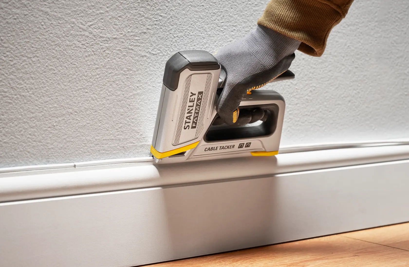 Stanley FMHT70100-0 Kabeltacker in Benutzung an der Fußleiste, von einer behandschuhten Hand gehalten.