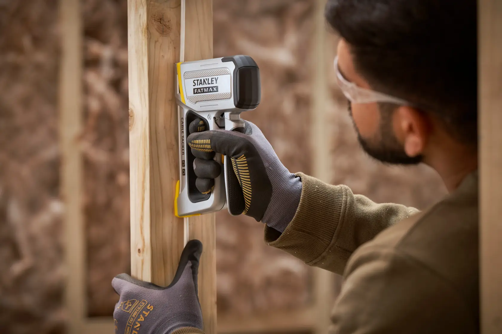 STANLEY FMHT70100-0 Ortungsgerät wird von behandschuhter Hand an einem Holzrahmen auf einer Baustelle gehalten.