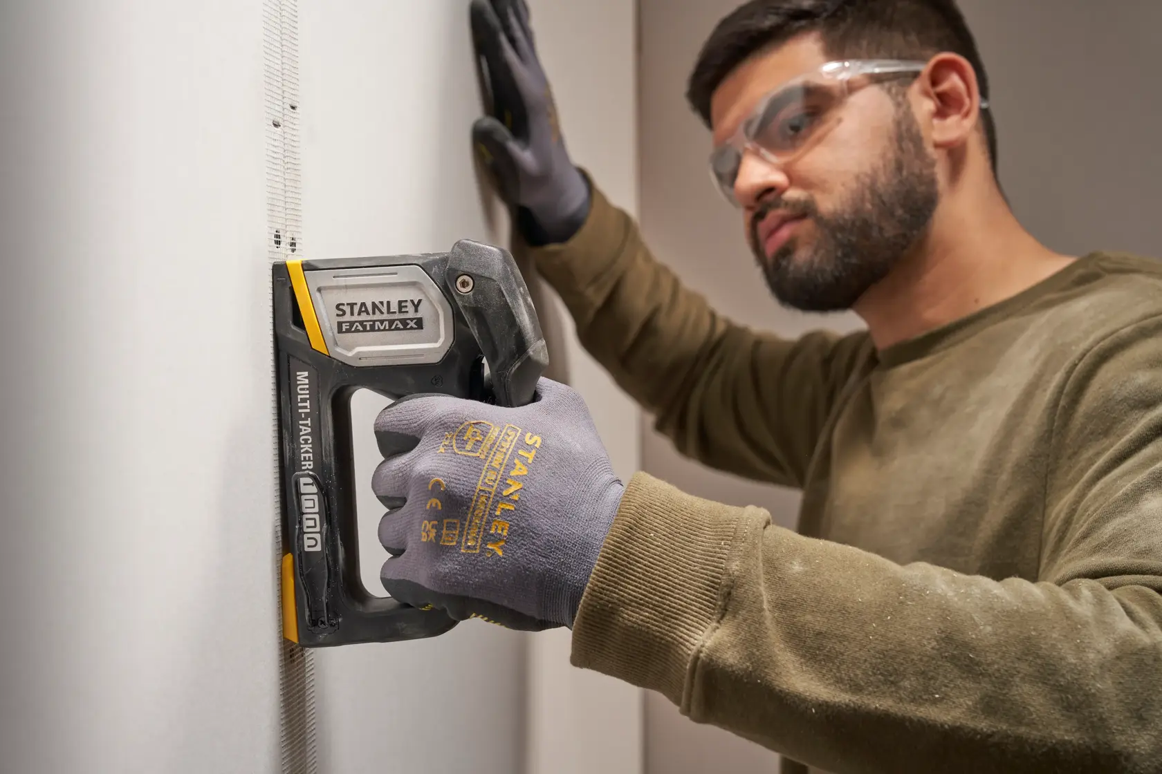 STANLEY FATMAX FMHT70401-0 Multitacker im Einsatz an Trockenbauwand von Person mit STANLEY Handschuhen, Seitenansicht.