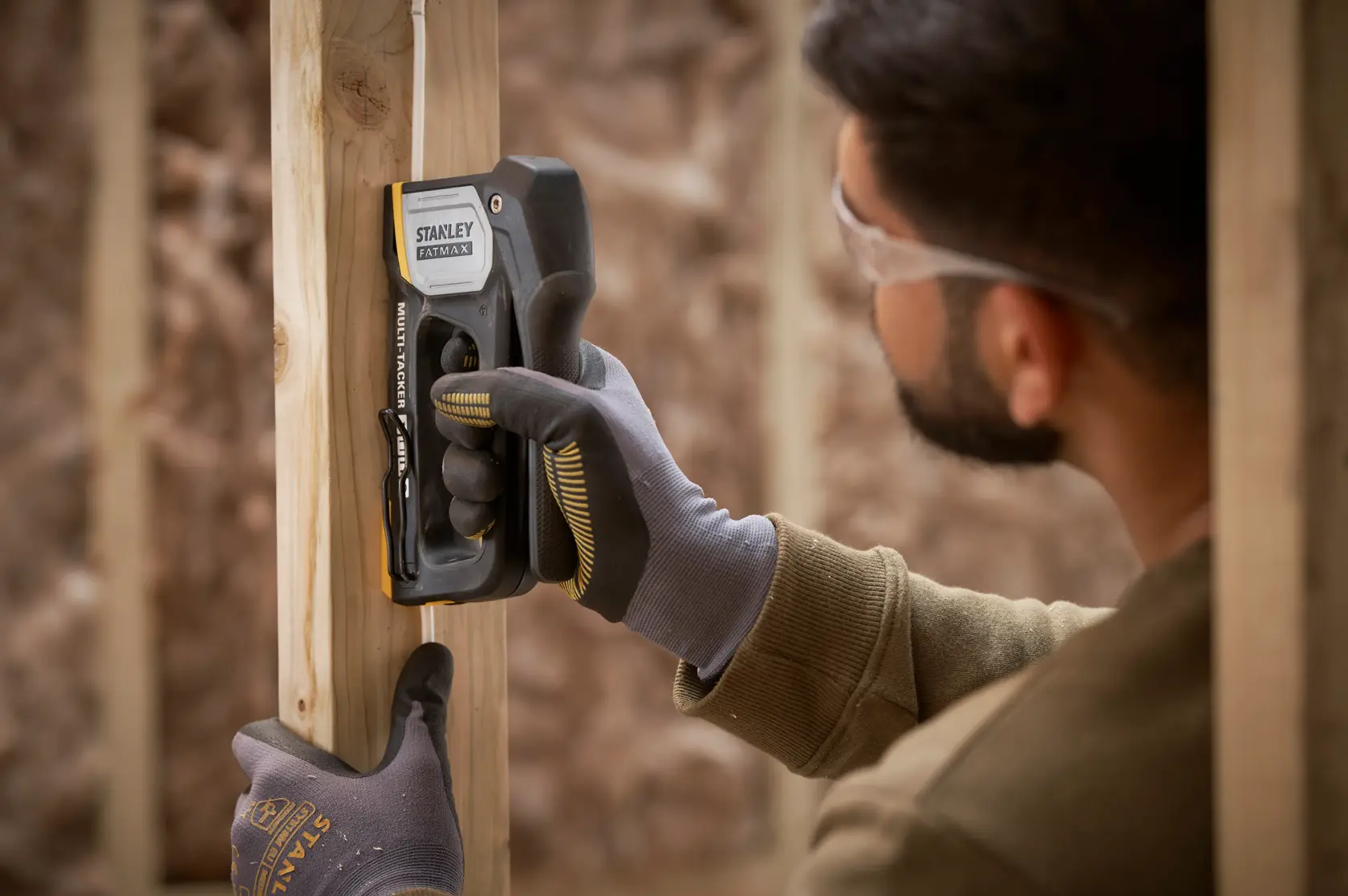 STANLEY FMHT70401-0 Tacker wird von behandschuhten Händen zum Befestigen eines Drahts am Holzrahmen verwendet.