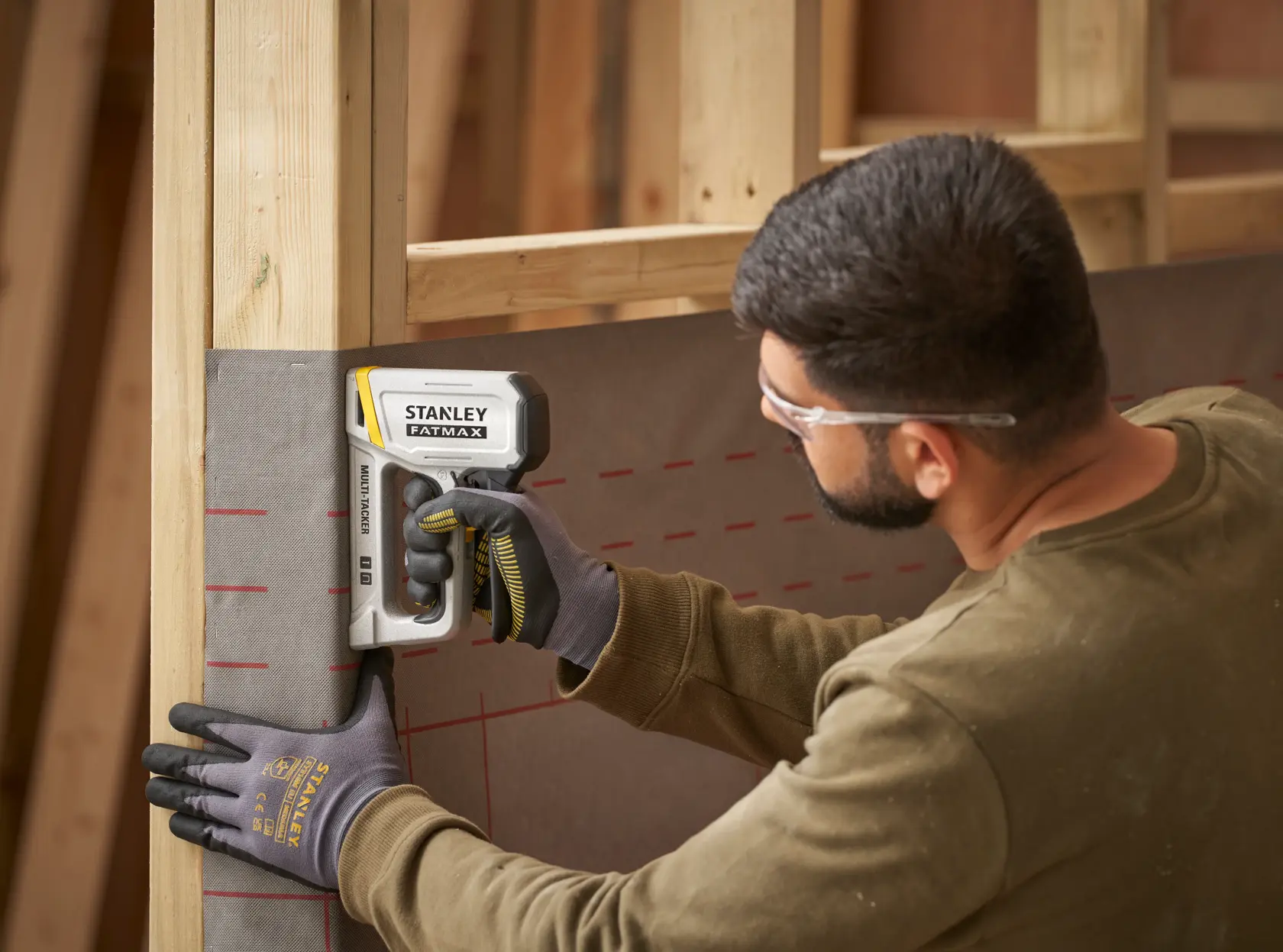 STANLEY FATMAX FMHT70443-0 Tacker, von einem Arbeiter mit Handschuhen zum Befestigen von Folie am Holzrahmen verwendet.