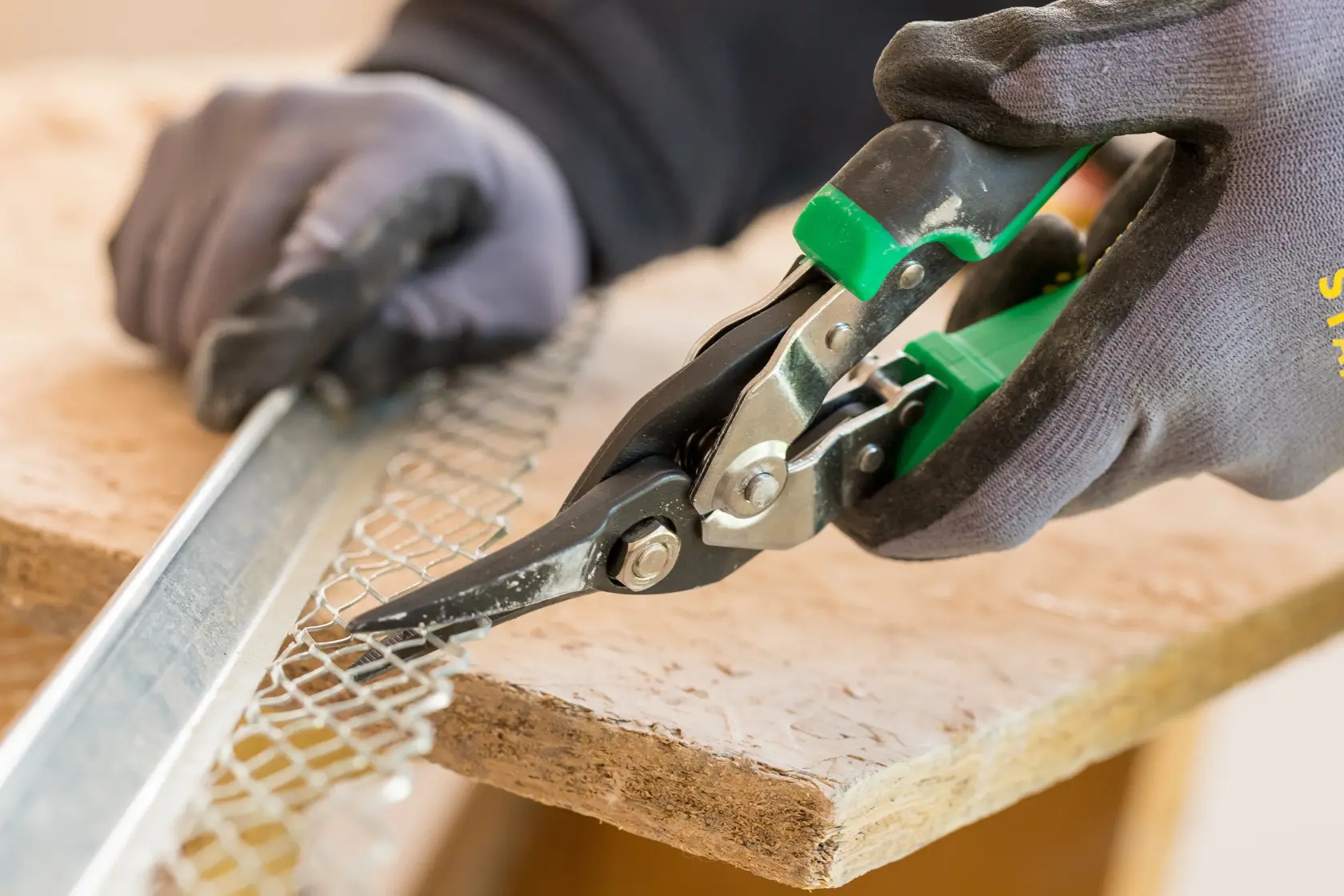 STANLEY FMHT73557-0 Fliegerblechschere schneidet Metallgitter, Nahaufnahme, Handschuh getragen.
