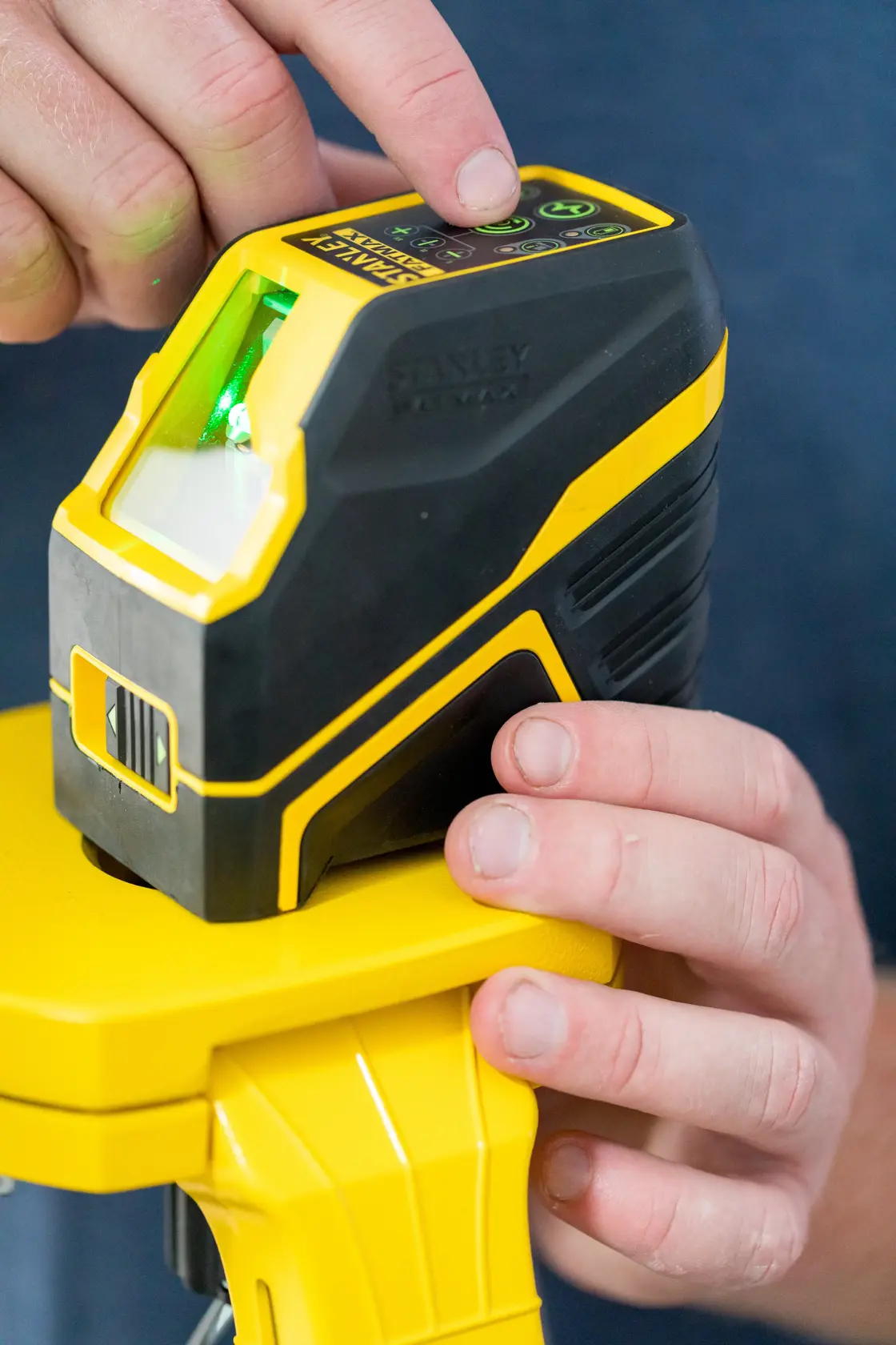 STANLEY FMHT77586-1 Kreuzlinien-Laser mit grünem Strahl auf Stativ, Nahaufnahme von Händen beim Bedienen der oberen Tasten.