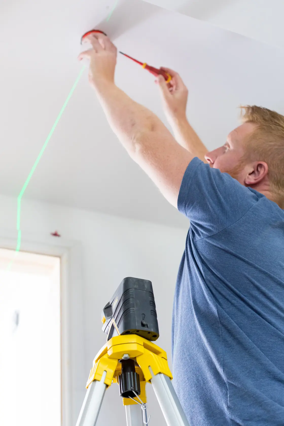 STANLEY FMHT77598-1 Laser-Nivelliergerät auf Stativ projiziert grüne Linie im Innenraum bei Deckenmontage.