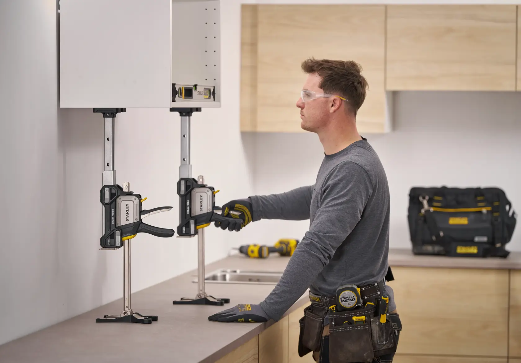 STANLEY FMHT83554-1 Schrankzwinge hält Hängeschrank bei der Montage, Arbeiter stellt die Zwinge in einer Küche ein.