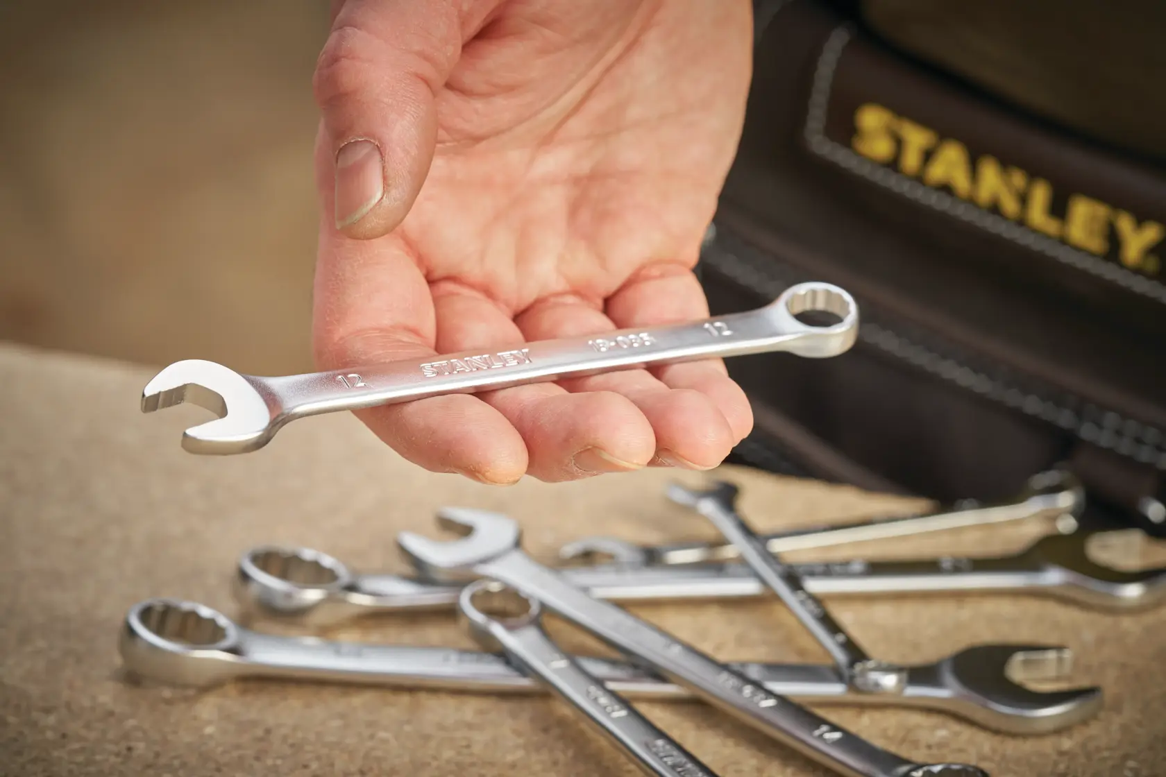 Stanley FMMT13036-0 Kombinationsschlüssel in der Hand gehalten, weitere Schlüssel auf Tisch, Nahaufnahme.