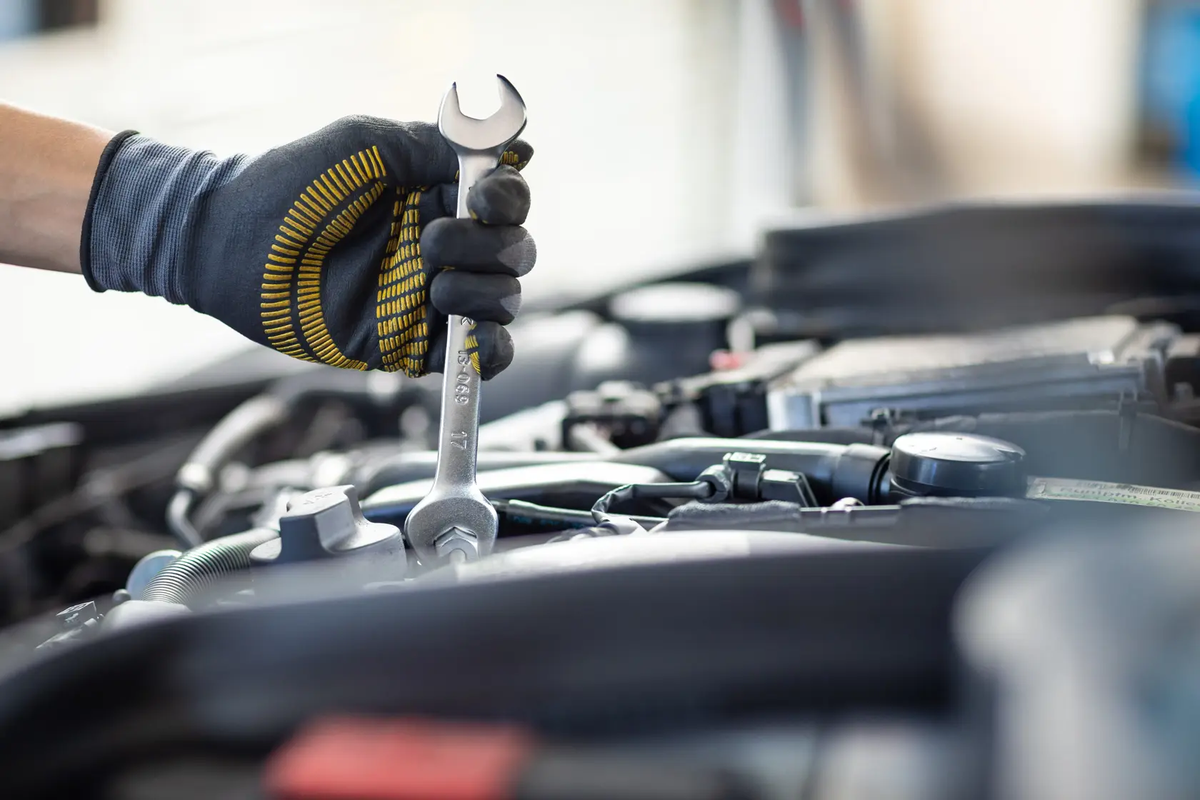 Foto von STANLEY FMMT13072-0 Schraubenschlüssel in behandschuhter Hand am Auto-Motor, Werkzeugdetails sichtbar.