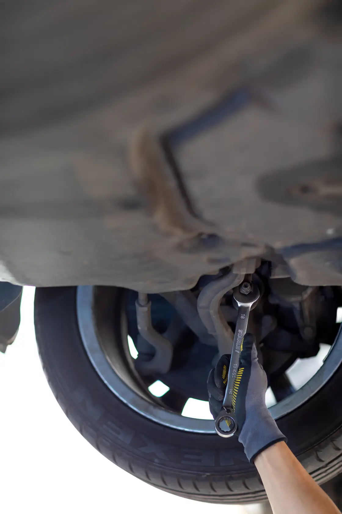 STANLEY FMMT13088-0 ratcheting wrench in use under car near wheel, held by gloved hand.
