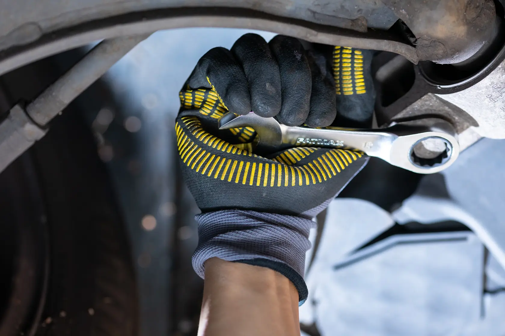 STANLEY FMMT13112-0 Schraubenschlüssel in behandschuhter Hand beim Festziehen eines Bolzens, Nahaufnahme Autoreparatur.