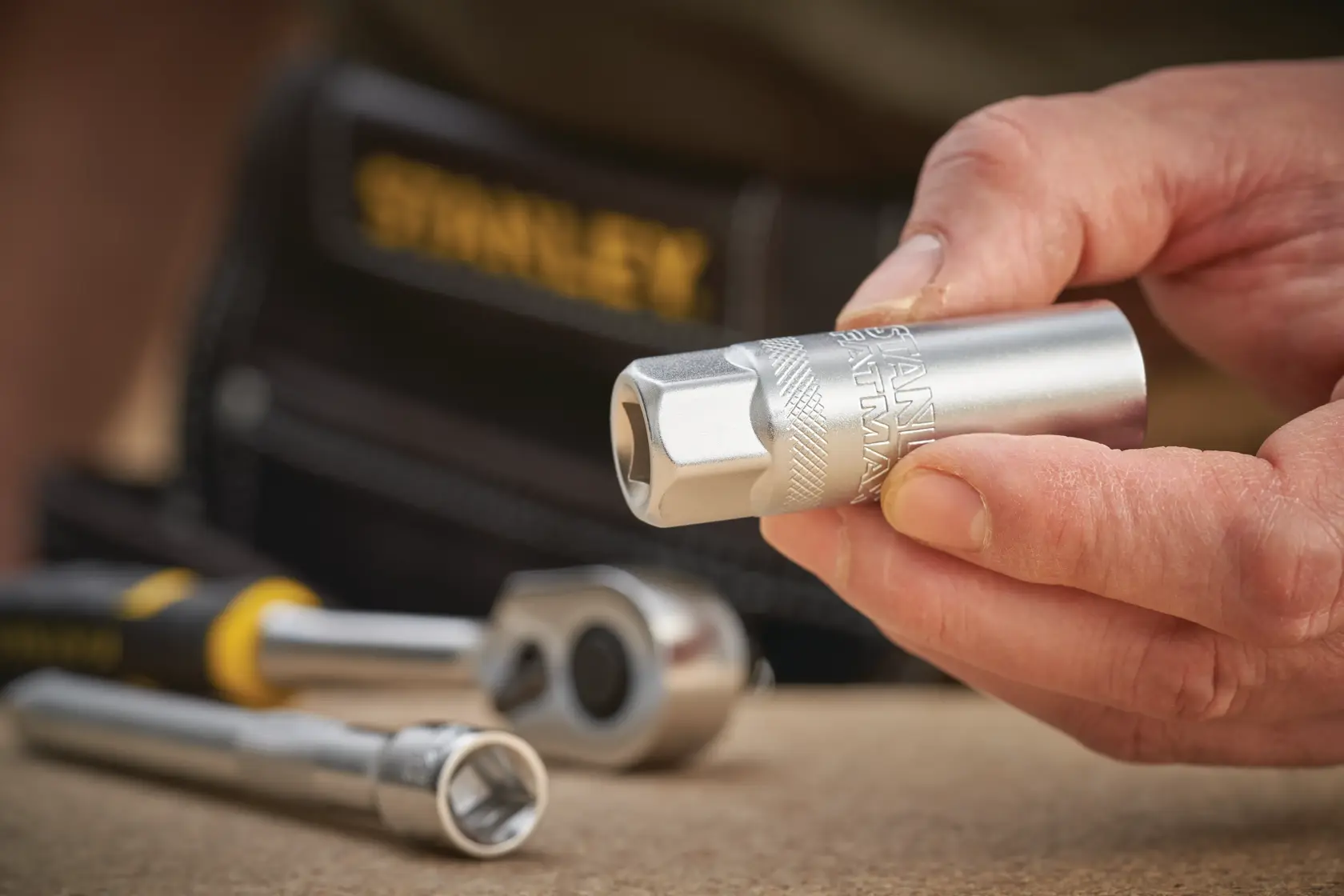 STANLEY FMMT17226-0 Steckschlüssel in der Hand, mit Ratsche und Verlängerung auf Werkfläche.