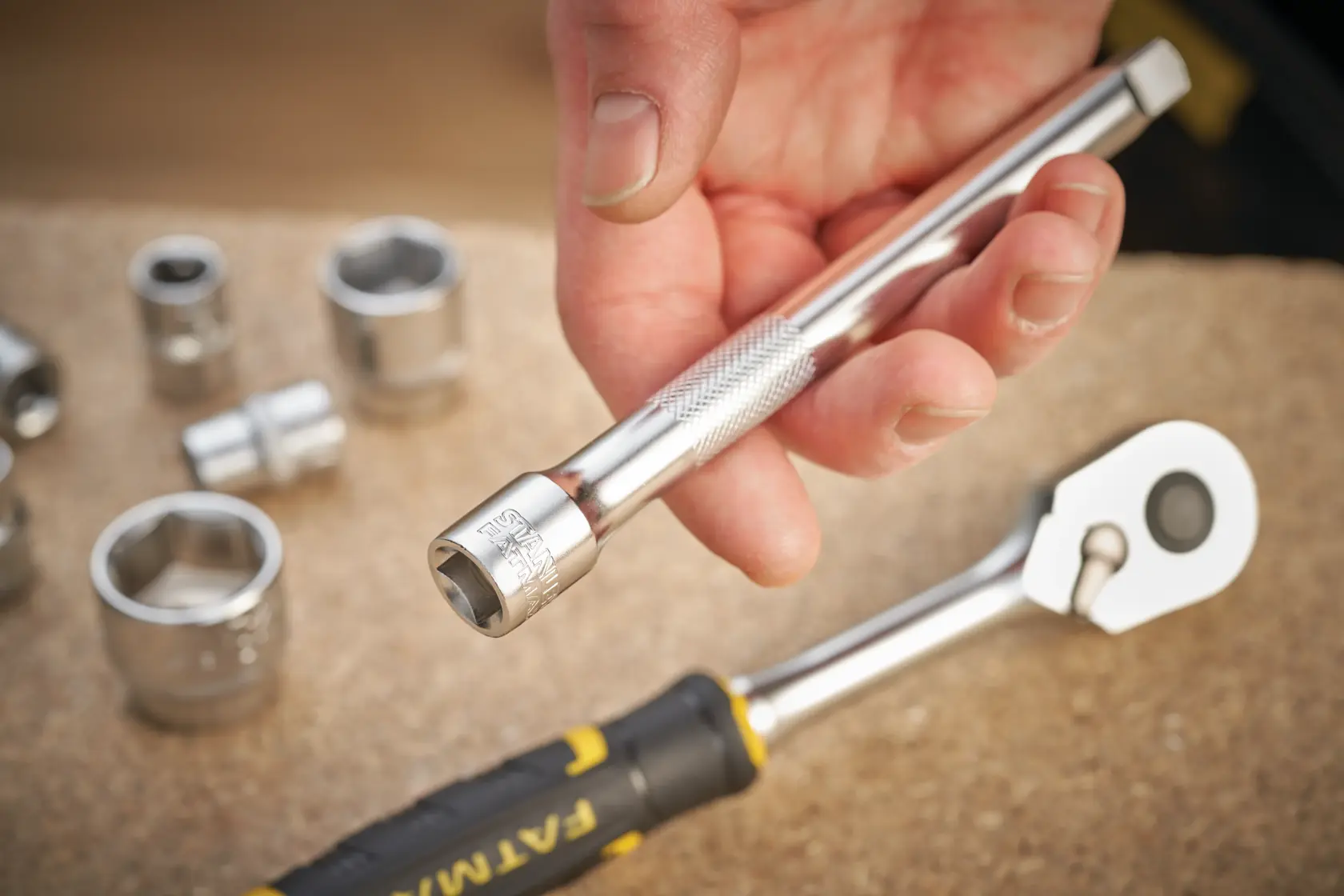 STANLEY FMMT25131-0 Verlängerungsstange für Steckschlüssel in der Hand, mit Chrom-Stecknüssen und Ratsche auf Werkbank.