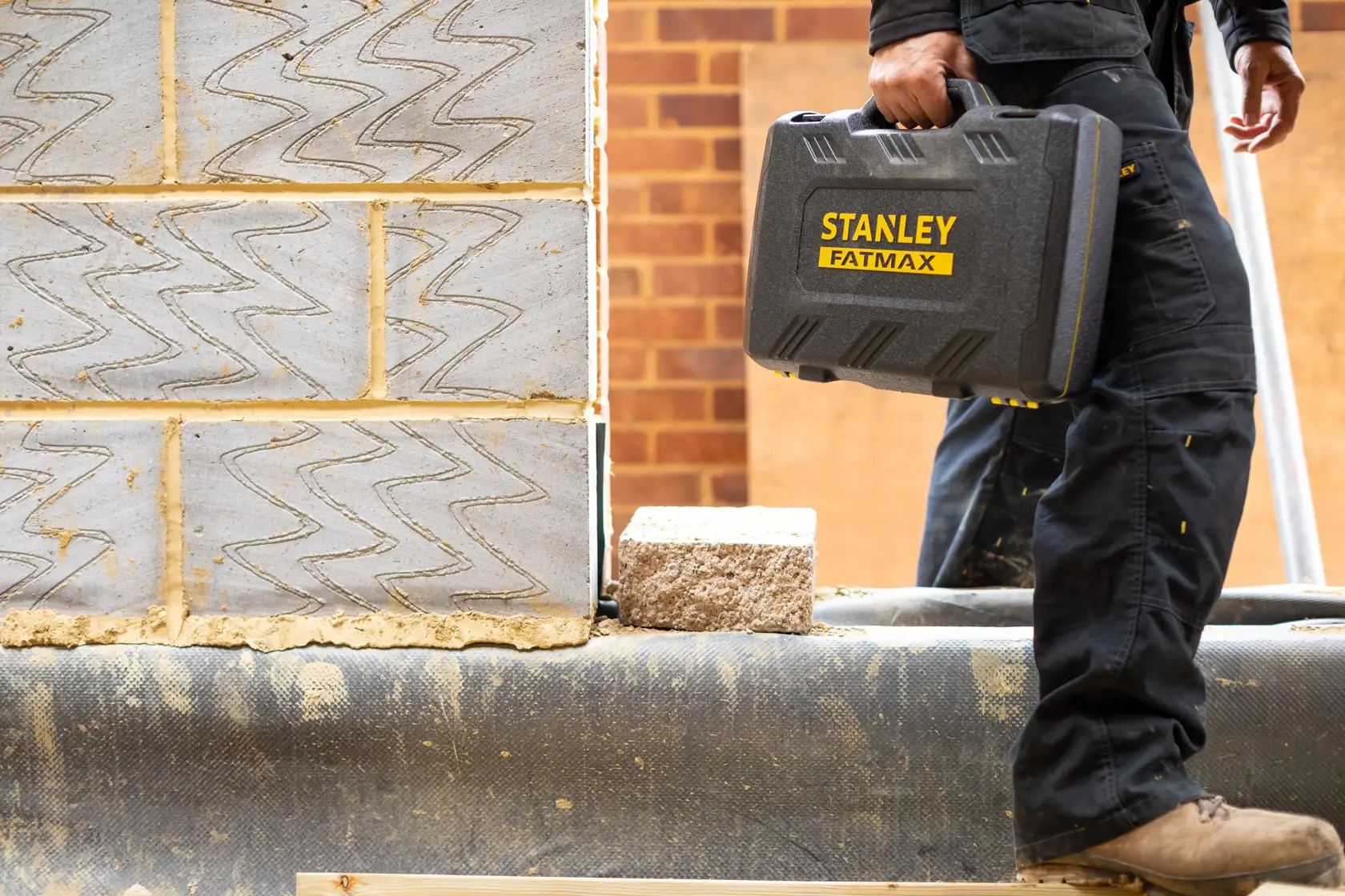 Foto eines Arbeiters, der einen STANLEY FATMAX FMMT82827-1 Werkzeugkoffer auf einer Baustelle trägt.