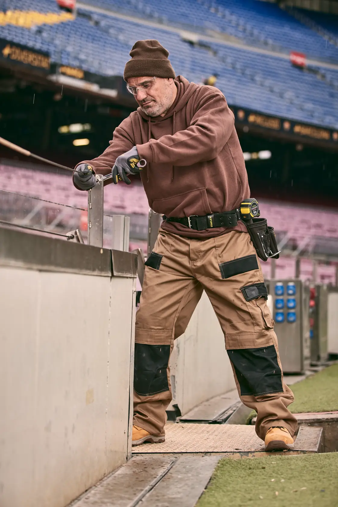 STANLEY FMMT82848-0 Profi mit Werkzeug, Werkzeuggürtel und Arbeitshose auf Baustelle im Stadion.