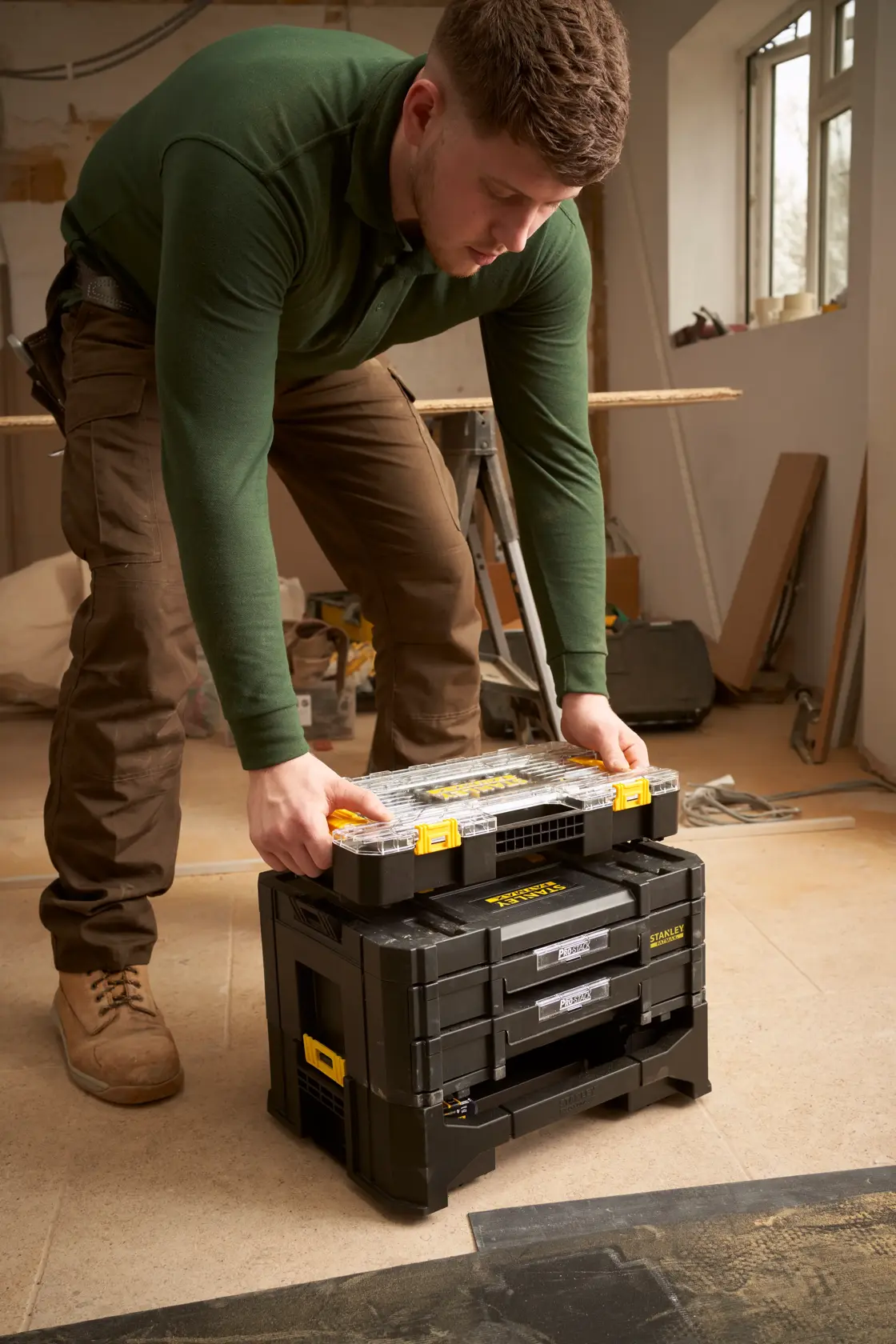 STANLEY FMMT98103-1 modulares schwarzes Werkzeugkastenset mit gelben Akzenten in Werkstatt, Person stapelt Organizer oben drauf.