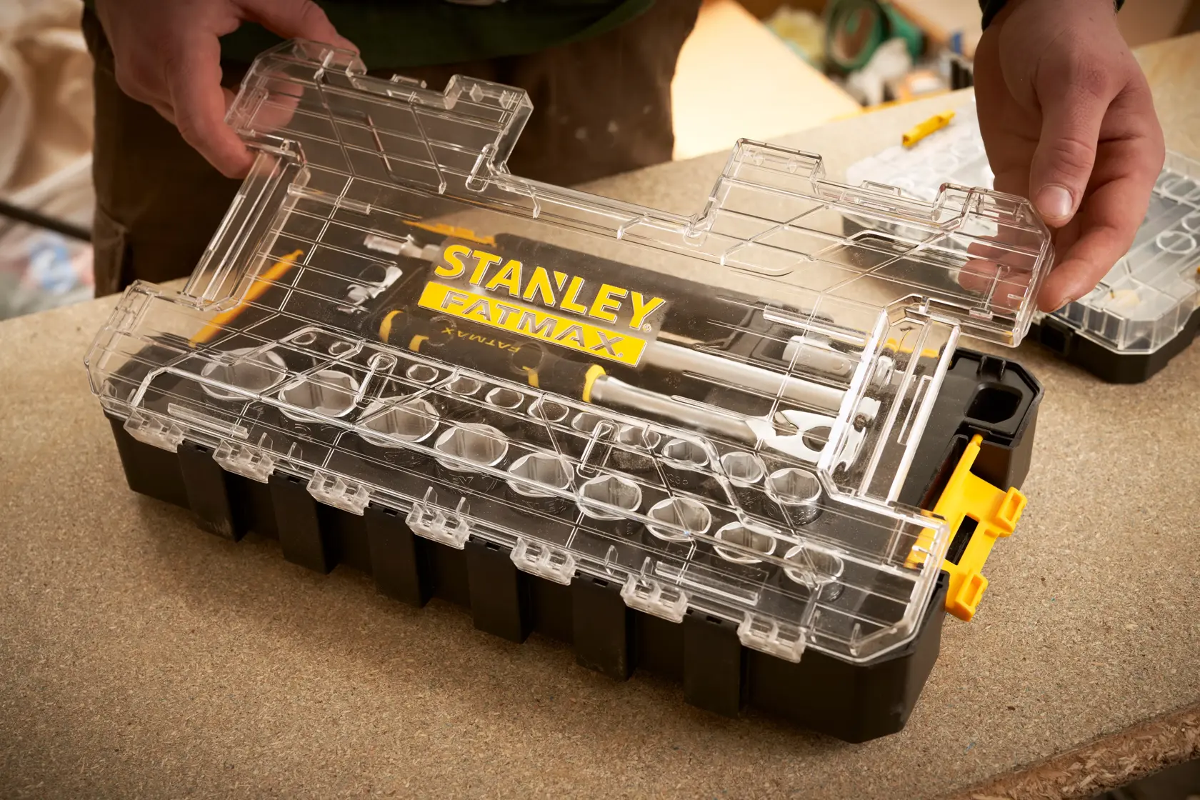STANLEY FMMT98103-1 Organizerbox mit klarem Deckel und FATMAX Branding, von Händen auf Werkbank gehalten.