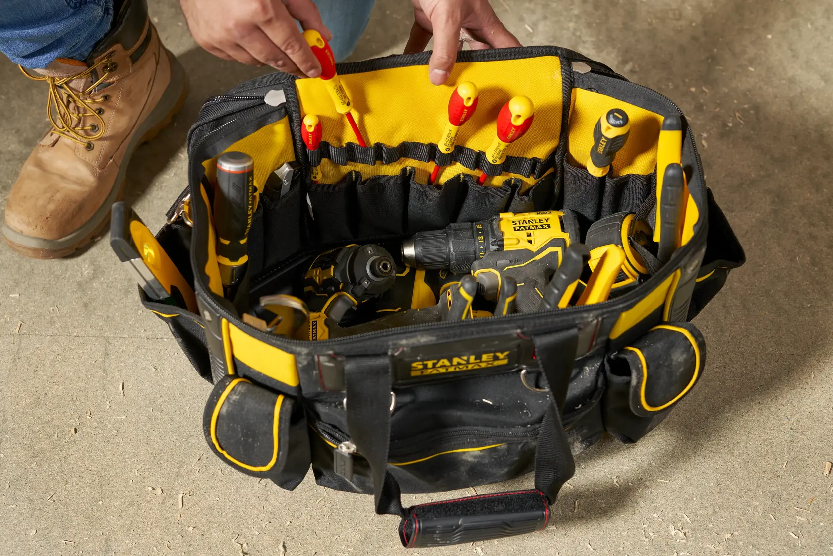 STANLEY FMST1-70749 offene Werkzeugtasche mit Handwerkzeugen und Bohrmaschine, Draufsicht auf Baustellenboden.