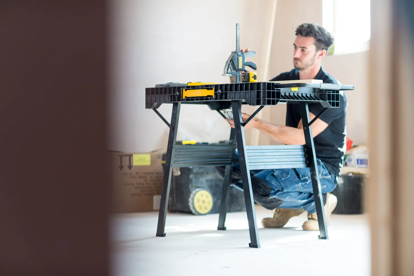Foto von STANLEY FMST1-75672 Werkbank im Einsatz auf Baustelle, Person kniet neben schwarzem Klapptisch.