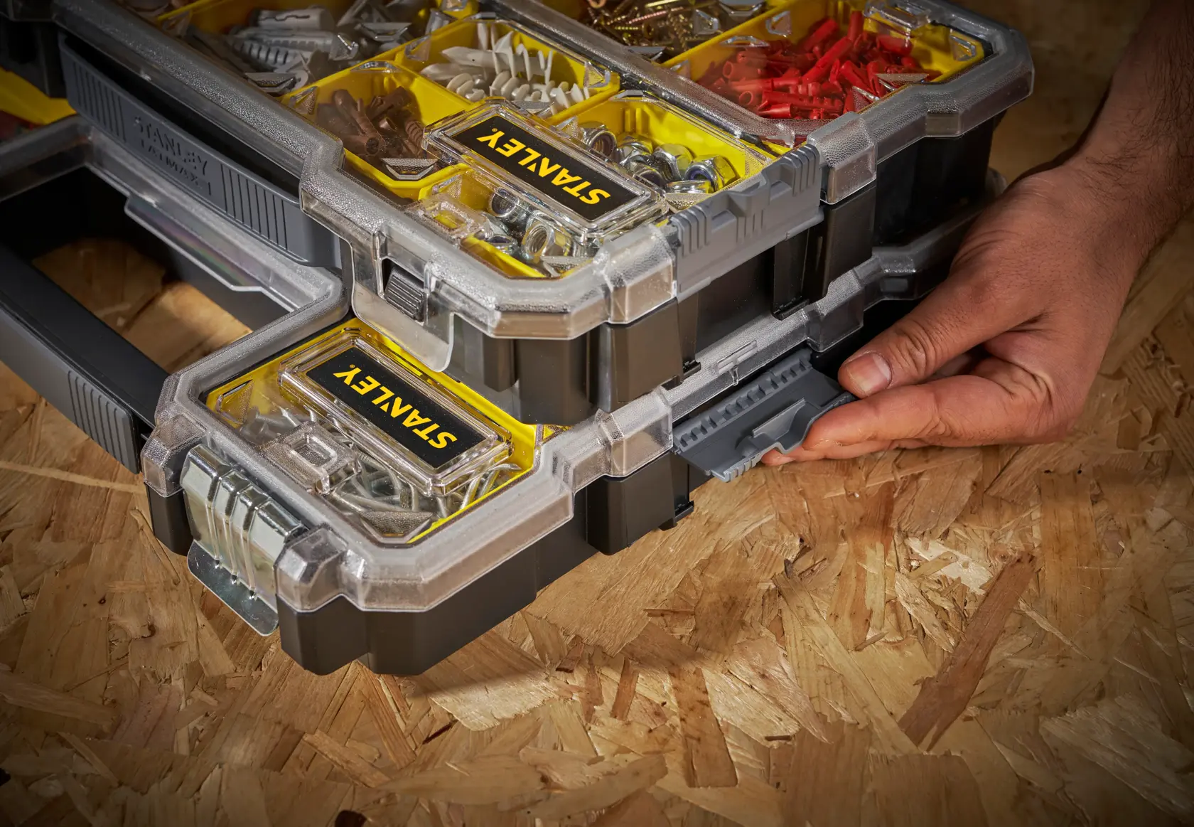 STANLEY FMST1-75779 stapelbarer Organizer mit gelben Fächern, Hand am Seitenverschluss, schräge Ansicht.