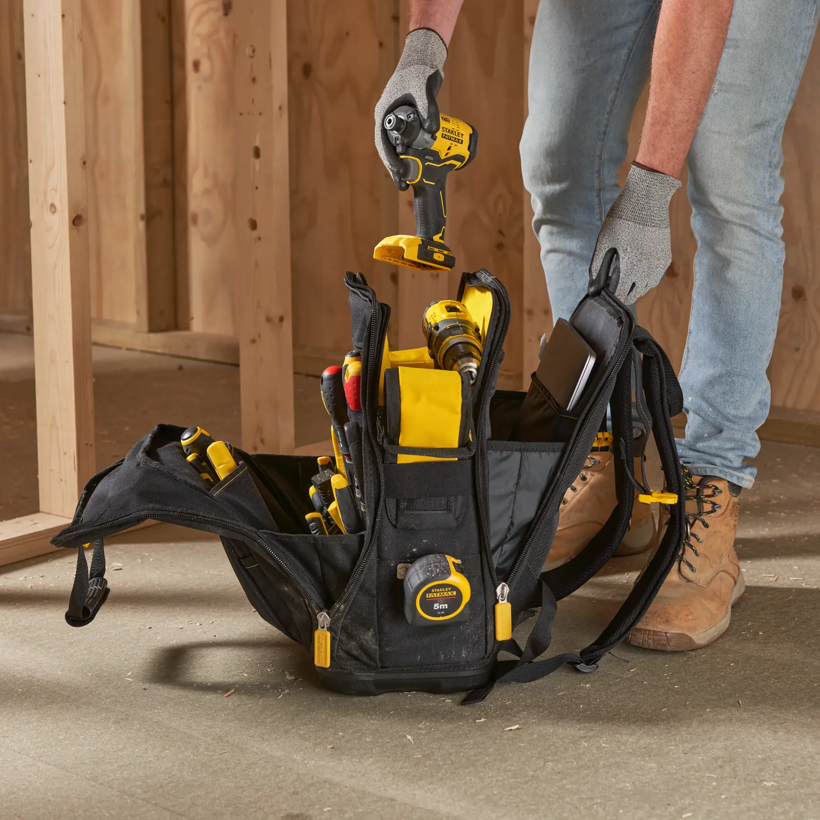 STANLEY FMST1-80144 Werkzeugrucksack mit Werkzeugen auf Baustelle, Person hält Bohrmaschine.