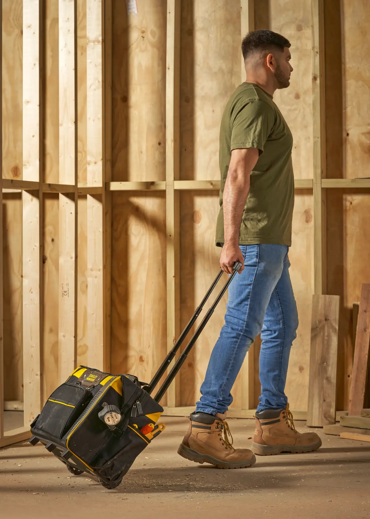 Stanley FMST1-80148 Rollwerkzeugtasche, von Mann auf Baustelle mit Holzwänden gezogen.