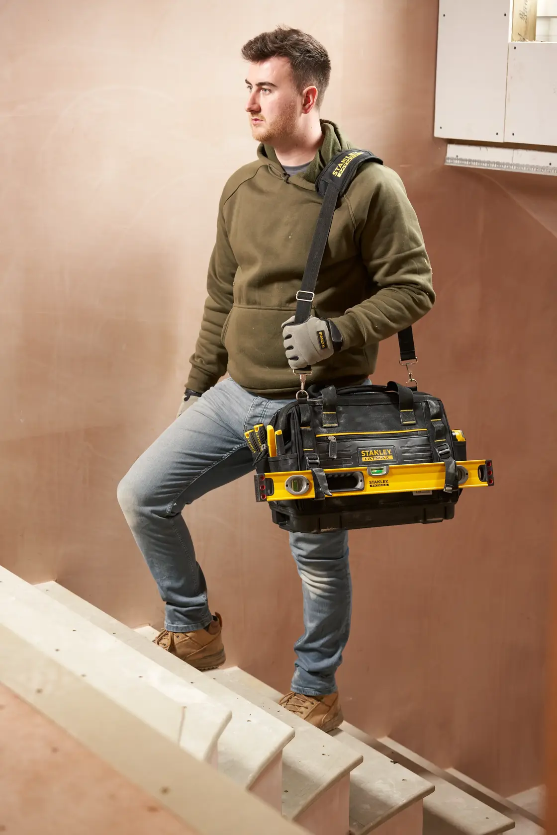 Stanley FMST17627-1 Werkzeugtasche mit gelben Akzenten, von Person auf Treppe über der Schulter getragen.