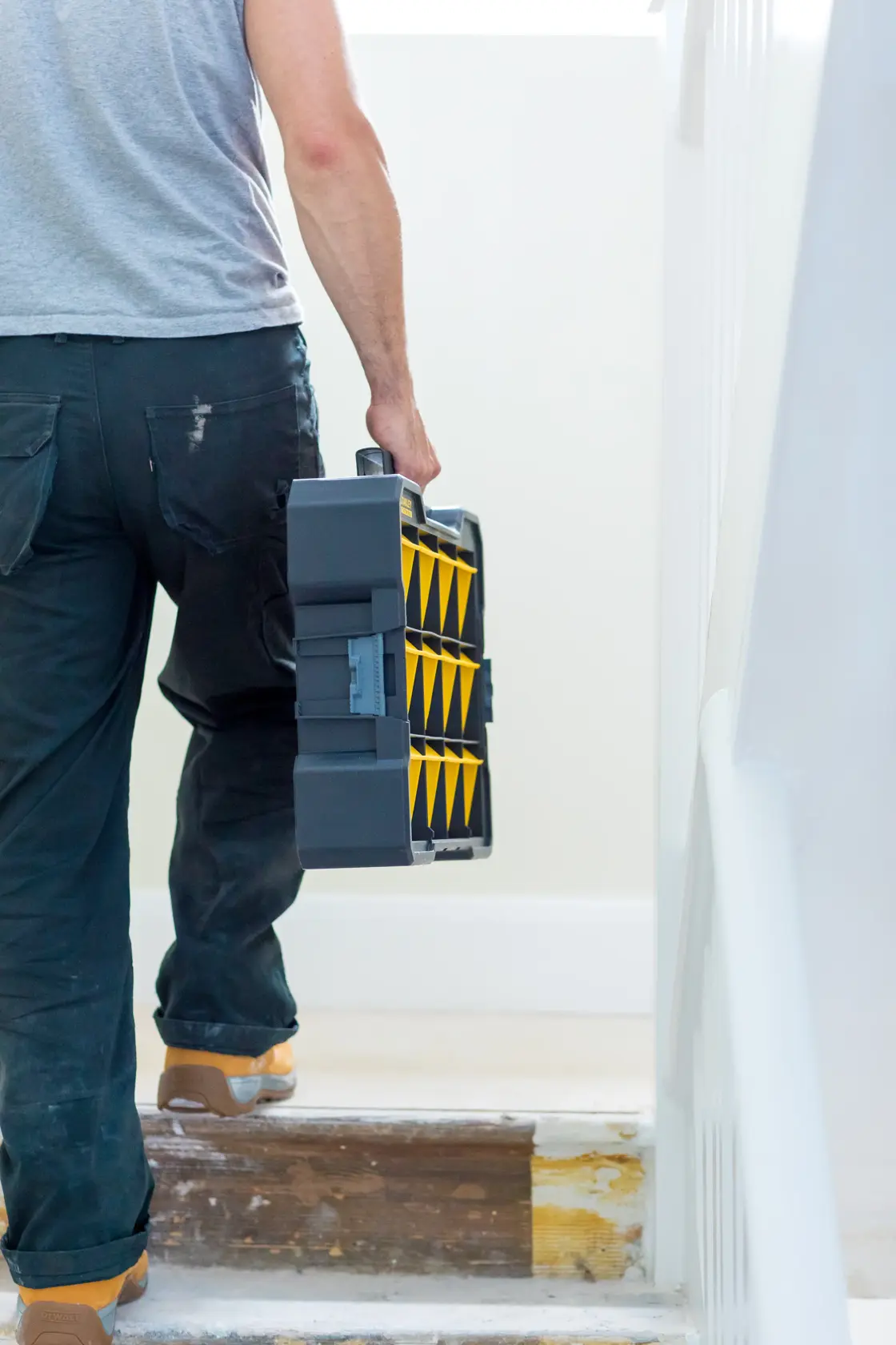 Foto einer Person, die einen STANLEY FMST81077-1 Werkzeug-Organizer mit gelben Fächern eine Treppe hinauf trägt.
