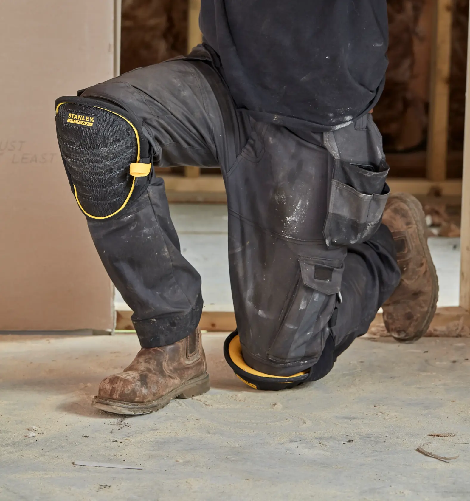 STANLEY FMST82959-1 schwarz-gelbes Knieschoner, getragen von einer knienden Person auf einer Baustelle.