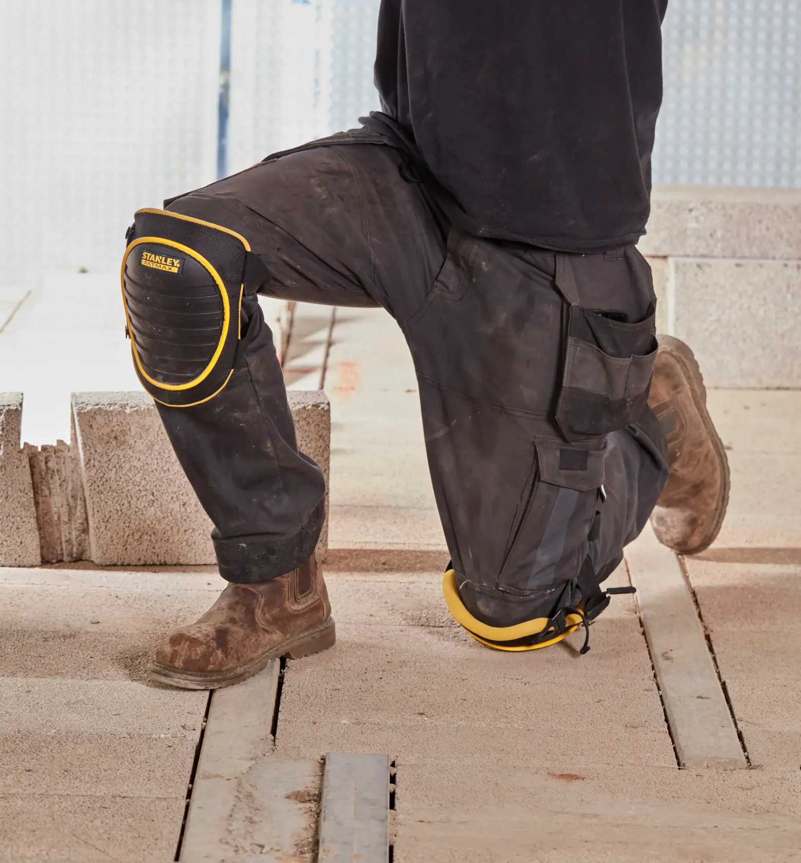 STANLEY FMST82961-1 Knieschoner, schwarz mit gelbem Rand, getragen über Arbeitshose auf Baustelle.