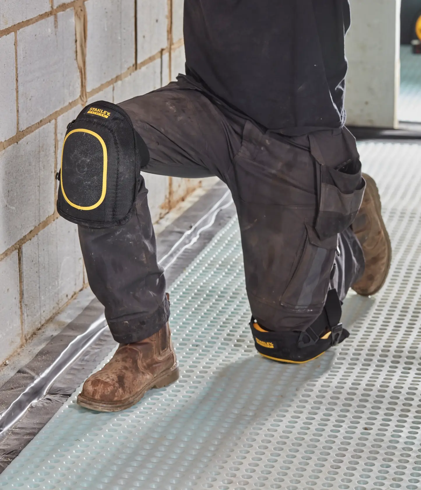 STANLEY FMST82962-1 Knieschoner, schwarz mit gelbem Rand, von Arbeiter auf Baustelle getragen.