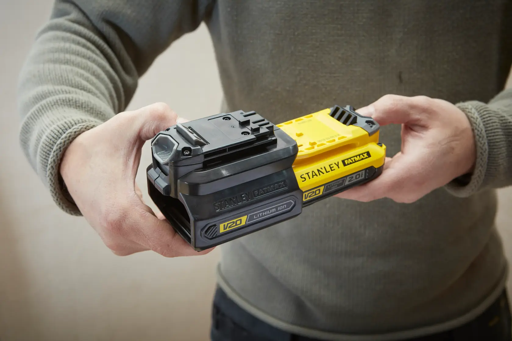 Foto von Händen, die STANLEY FATMAX SFMCB100 V20 Lithium-Ionen-Akkus halten, einer schwarz und einer gelb.