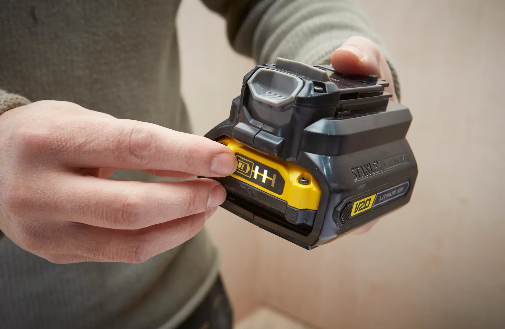 Fotografie der STANLEY SFMCB121D1 V20 Lithium-Ionen-Batterie, Nahaufnahme in der Hand, gelbes Anzeigenfeld.