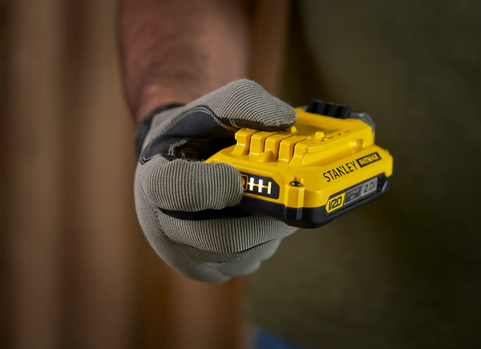 Foto von STANLEY SFMCB12D2 gelber V20 Batterie in einer behandschuhten Hand, Produktfotografie Nahaufnahme.