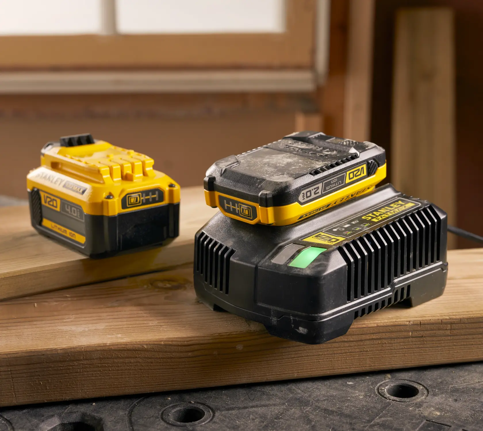 Foto des STANLEY SFMCB14 V20 Lithium-Ionen-Akkus und Ladegeräts auf Holz im Werkstattumfeld.