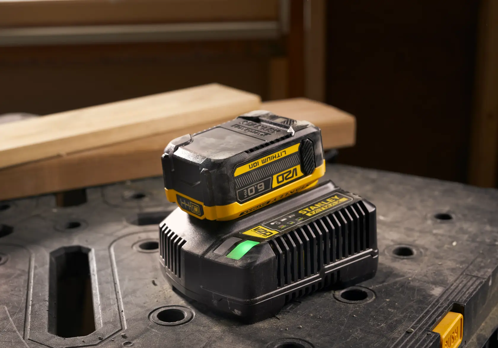 Stanley SFMCB206 Lithium-Ionen-Akku und Ladegerät auf Werkbank, Fotografie aus Frontalperspektive.